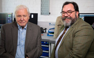 Dr Neil Gostling, a smiling, bearded scientist, sits next to Sir David Attenborough.
